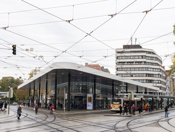 A modern building with a curved glass facade and a tram station in front. - Limehome Augsburg Annastraße (Augsburg)