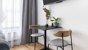 Una habitación moderna con televisión de pantalla plana en la pared, una pequeña mesa con dos sillas y una planta en maceta.