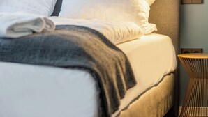 Una cama con ropa blanca, un cabecero gris y una mesita de noche con una lámpara.