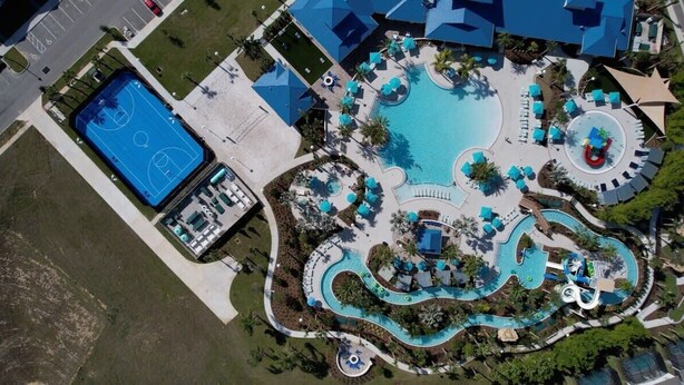 An aerial view of a resort with a central pool, a tennis court, and a water slide.