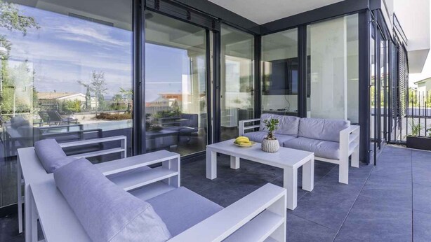 A modern outdoor living space with glass doors, white furniture, and a view of the surrounding area. - Villa with private pool, jacuzzi and sauna (Malinska)