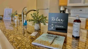 Una encimera de cocina con un cartel que dice 'Relájate y disfruta del wifi', una planta en maceta, una botella de desinfectante y un folleto de bienvenida.