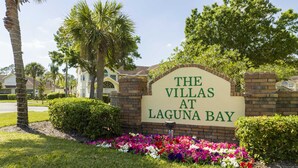Señal que indica "The Villas at Laguna Bay", con un muro de ladrillo y un parterre floral al frente.