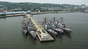A large naval ship docked at a port with a cityscape in the background. - Attract travellers with an engaging headline (Columbus)