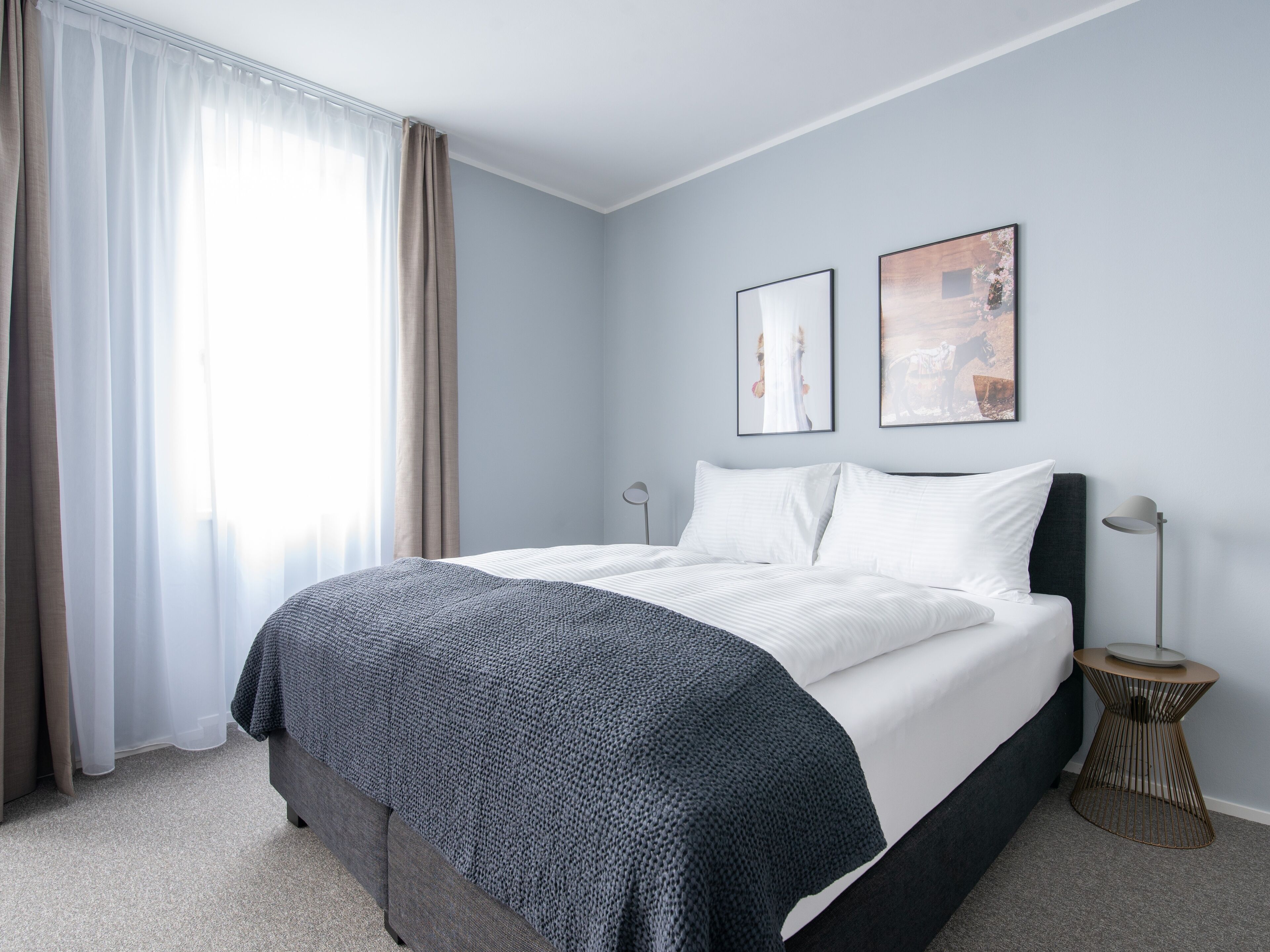 Una habitación de hotel moderna con una cama grande, una mesita auxiliar y dos cuadros enmarcados en la pared.