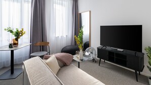 A modern living room with a sofa, a TV, a fan, and a table with a vase of flowers. - Limehome Linz Friedrichstraße (Linz)