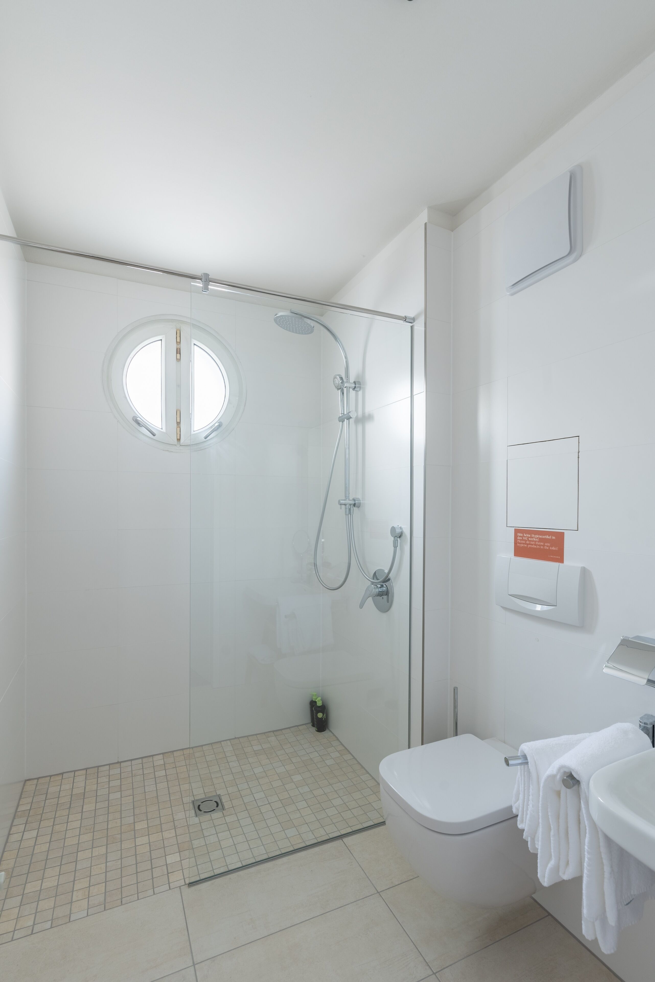 A modern bathroom with a glass-enclosed shower, a toilet, and a sink with a towel rack.