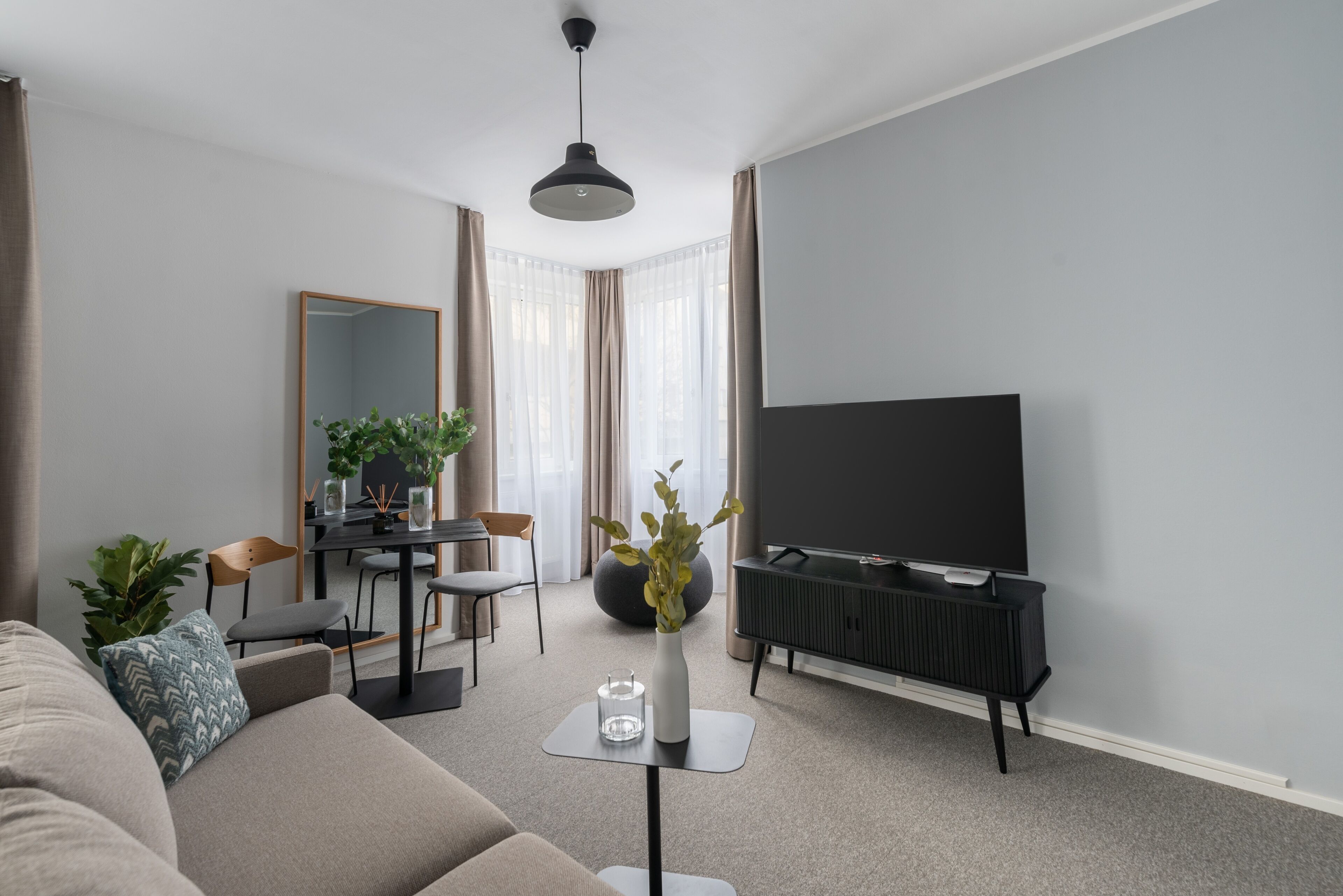 Un soggiorno moderno con un divano, un tavolino, una televisione, un'area pranzo con sedie e un grande specchio.