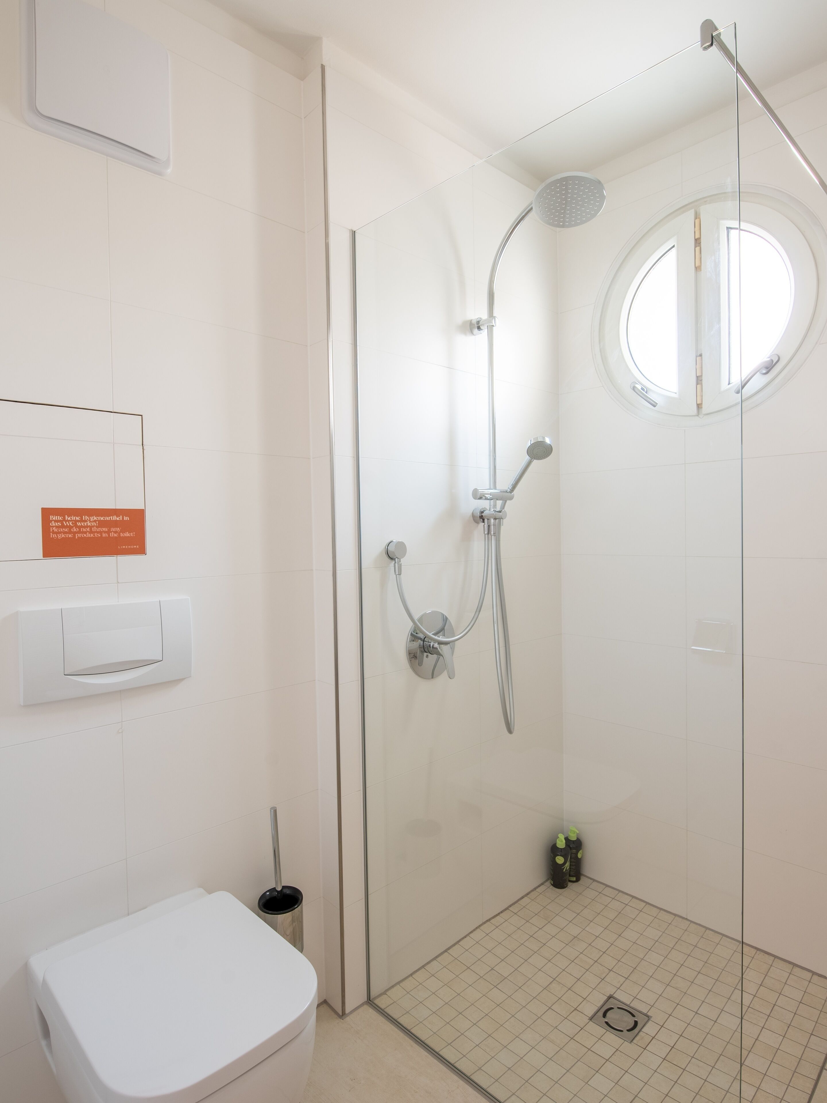A modern bathroom with a glass-enclosed shower, a toilet, and a hand dryer.
