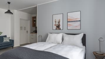 Un dormitorio moderno con una cama grande, un escritorio y una silla. Hay dos cuadros en la pared.