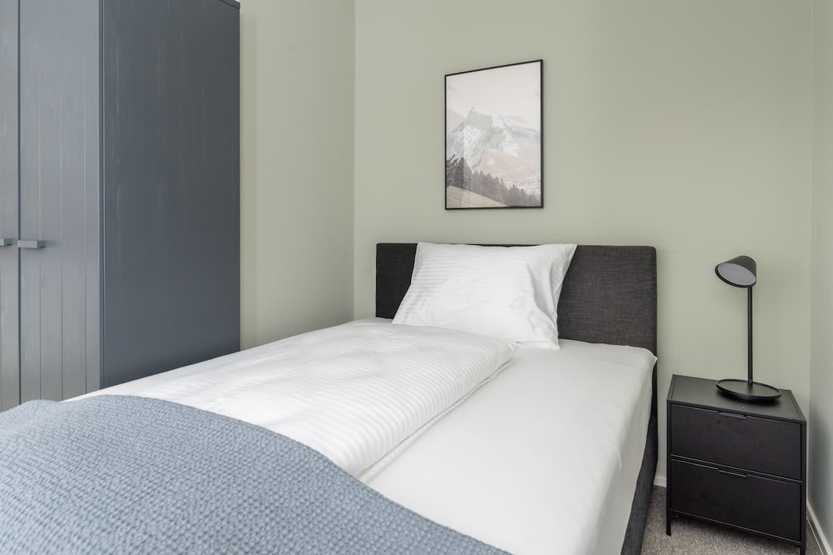 A bedroom with a bed, a nightstand, a lamp, a wardrobe, and a framed picture on the wall.