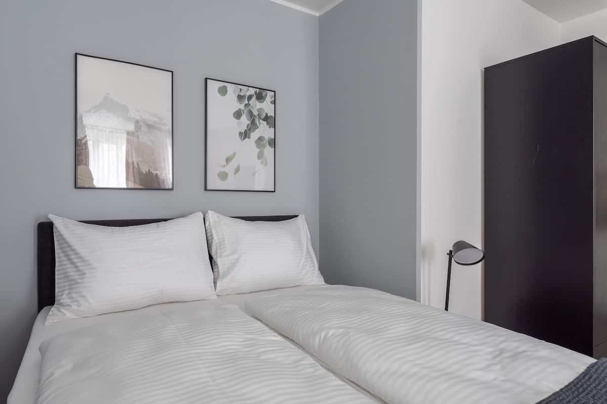 A neatly made bed with white linens and two pillows, a dark headboard, and two framed pictures on the wall.