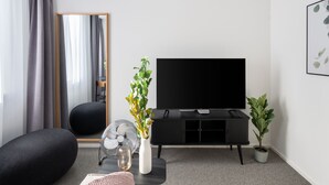 A modern living room with a flat-screen TV, black sofa, and a potted plant. - Limehome Linz Friedrichstraße (Linz)