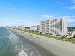 A beachfront hotel with multiple floors, a sandy beach, and a clear sky.