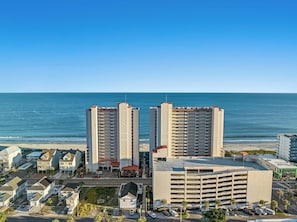 A coastal cityscape with two prominent high-rise buildings, a parking garage, and a beach in the background.