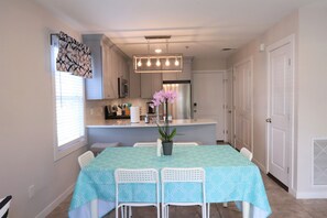 A dining area with a table set for four, a kitchen in the background, and a potted plant on the table.
