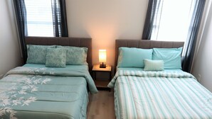 A bedroom with two beds, each with a different patterned bedspread, a bedside table with a lamp, and a window with curtains. - ★GORGEOUS STYLISH APT Close to American Dream & NYC★ (Belleville)