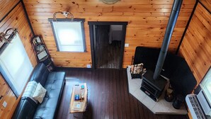 Interno di una baita in legno con soffitto spiovente, un lucernario esagonale centrale, un camino, un divano, un tavolino da caffè e una scala che conduce al piano superiore.