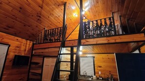 Una baita di legno con un soppalco, una scala e un balcone con ringhiera in metallo.