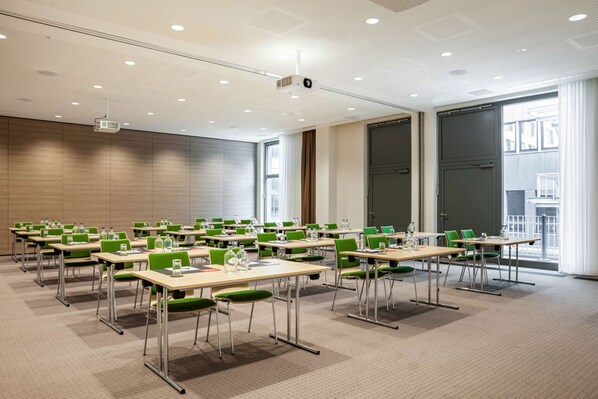 A conference room with multiple tables and chairs, large windows, and a projector on the ceiling.
