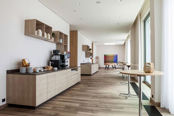 Una cocina moderna con armarios de madera, una estación de café y un cuadro de colores en la pared.