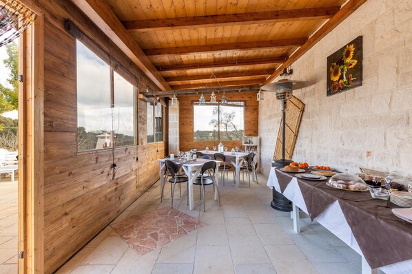Un intérieur en bois avec des tables dressées pour le repas, une grande fenêtre et un tableau accroché au mur.