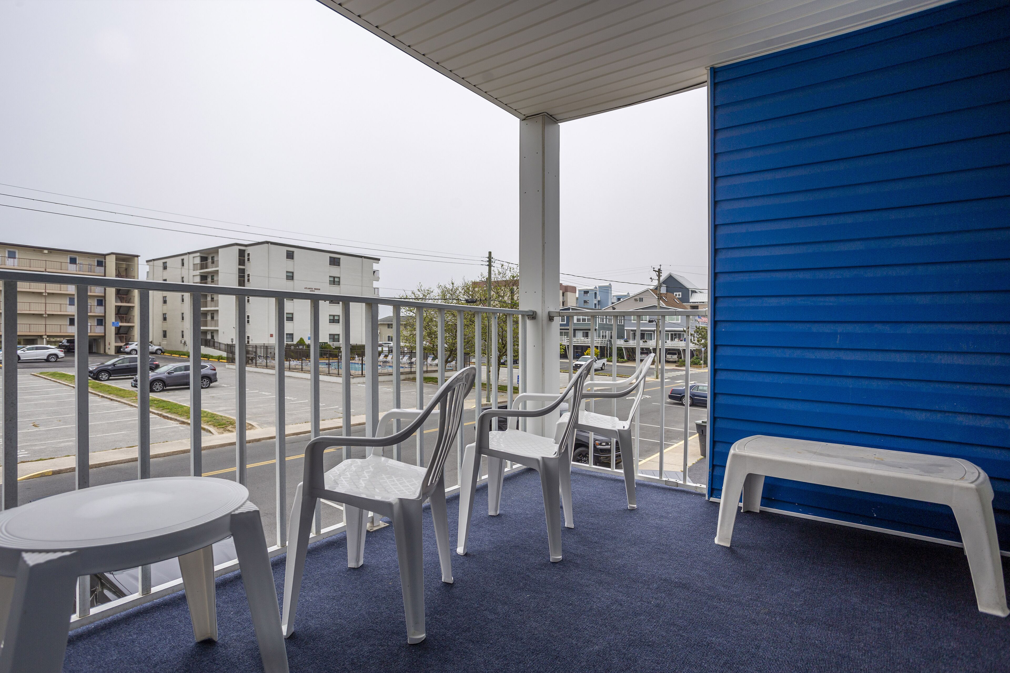 A balcony with plastic chairs and a bench, overlooking a street with cars and buildings.