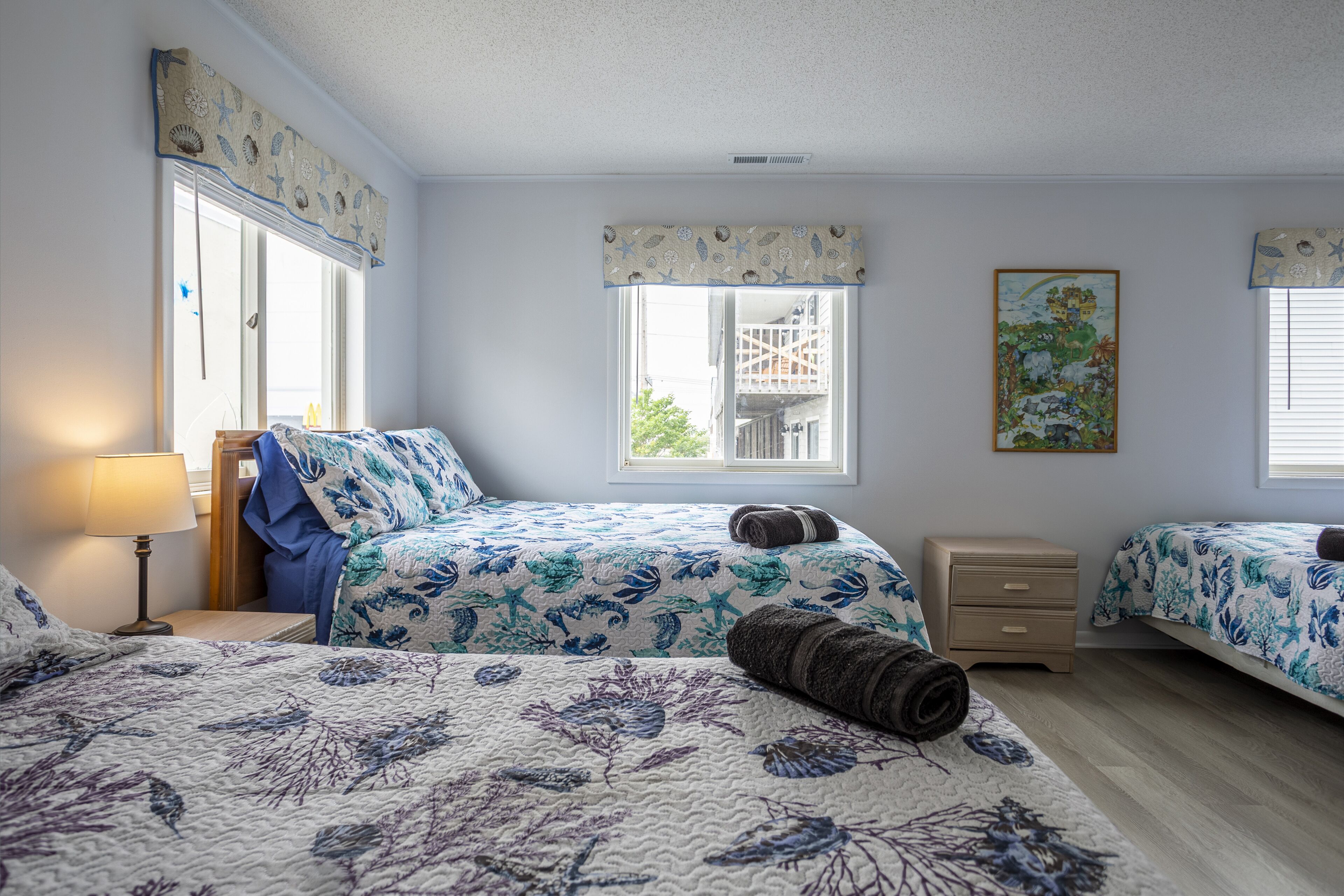 A bedroom with two beds, a nightstand, a lamp, and a window with a view of a balcony.