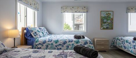A bedroom with two beds, a nightstand, a lamp, and a window with a view of a balcony.