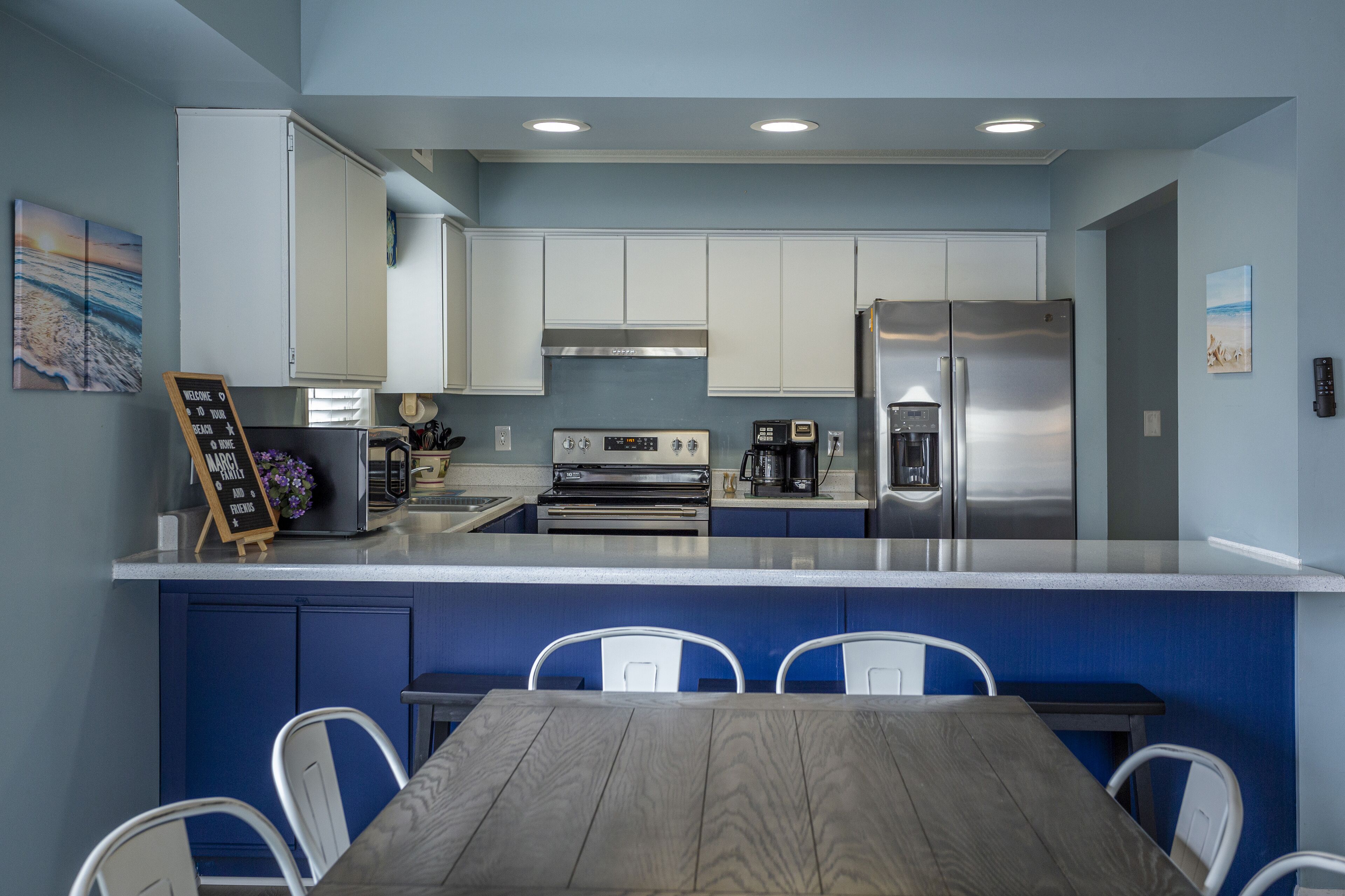 A modern kitchen with white cabinets, a stainless steel refrigerator, a built-in oven, and a dining area with a wooden table and white chairs.