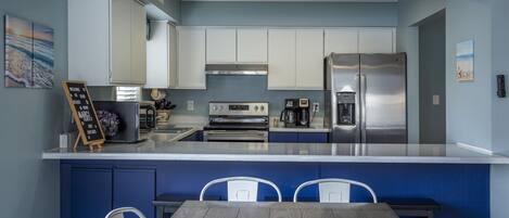A modern kitchen with white cabinets, a stainless steel refrigerator, a built-in oven, and a dining area with a wooden table and white chairs.