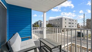 Ein Balkon mit einer Sitzbank, einem weißen Geländer und Blick auf ein mehrgeschossiges Gebäude im Hintergrund.