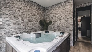 Une salle de bain moderne avec un mur décoré d’un motif imitant la pierre, une baignoire sur pieds et une porte visible donnant sur une autre pièce.