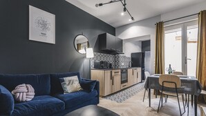 Un salon moderne avec un canapé bleu, une table à manger avec des chaises, un coin cuisine et une grande fenêtre avec des rideaux.