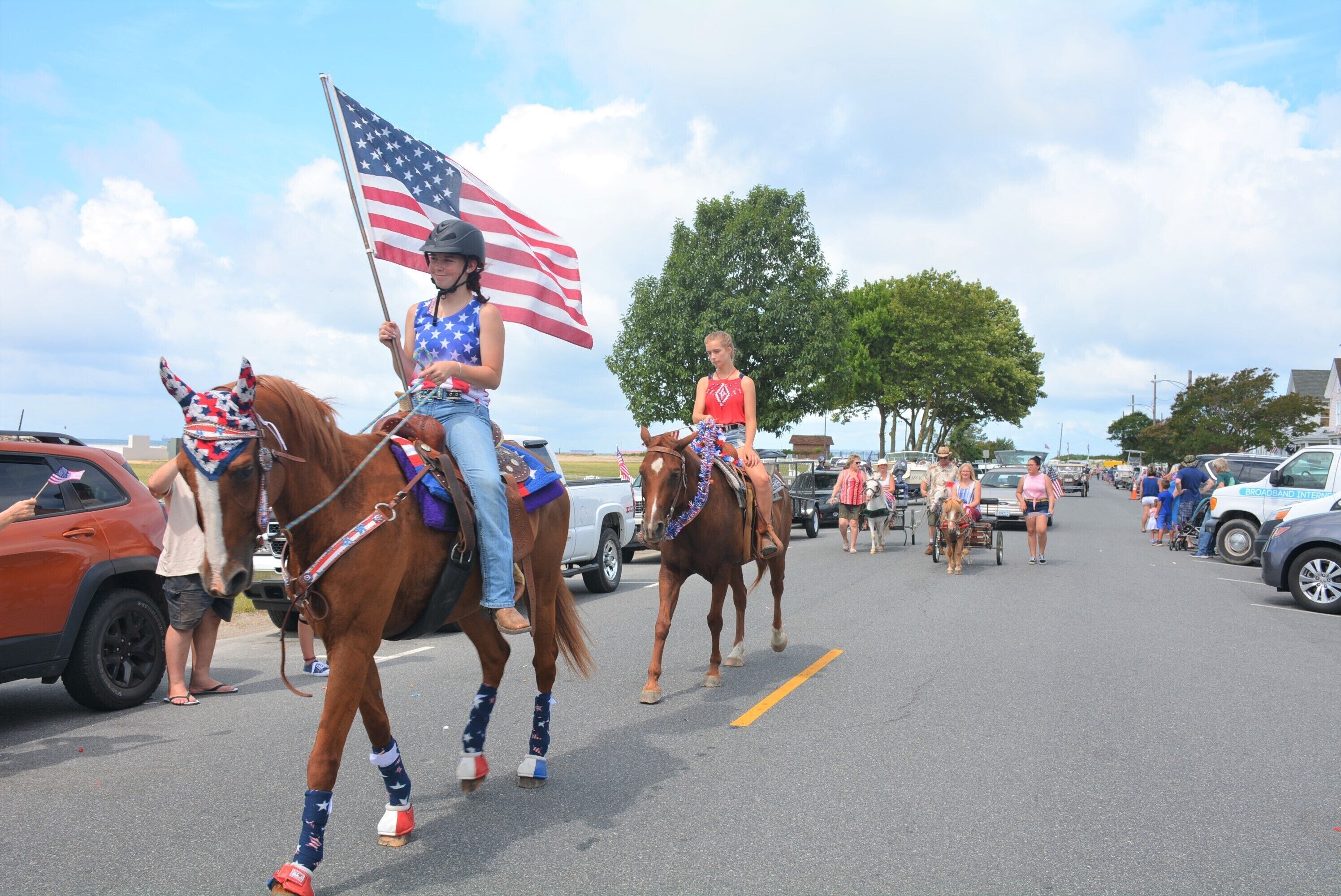 A parade with people riding horses, some holding American flags.