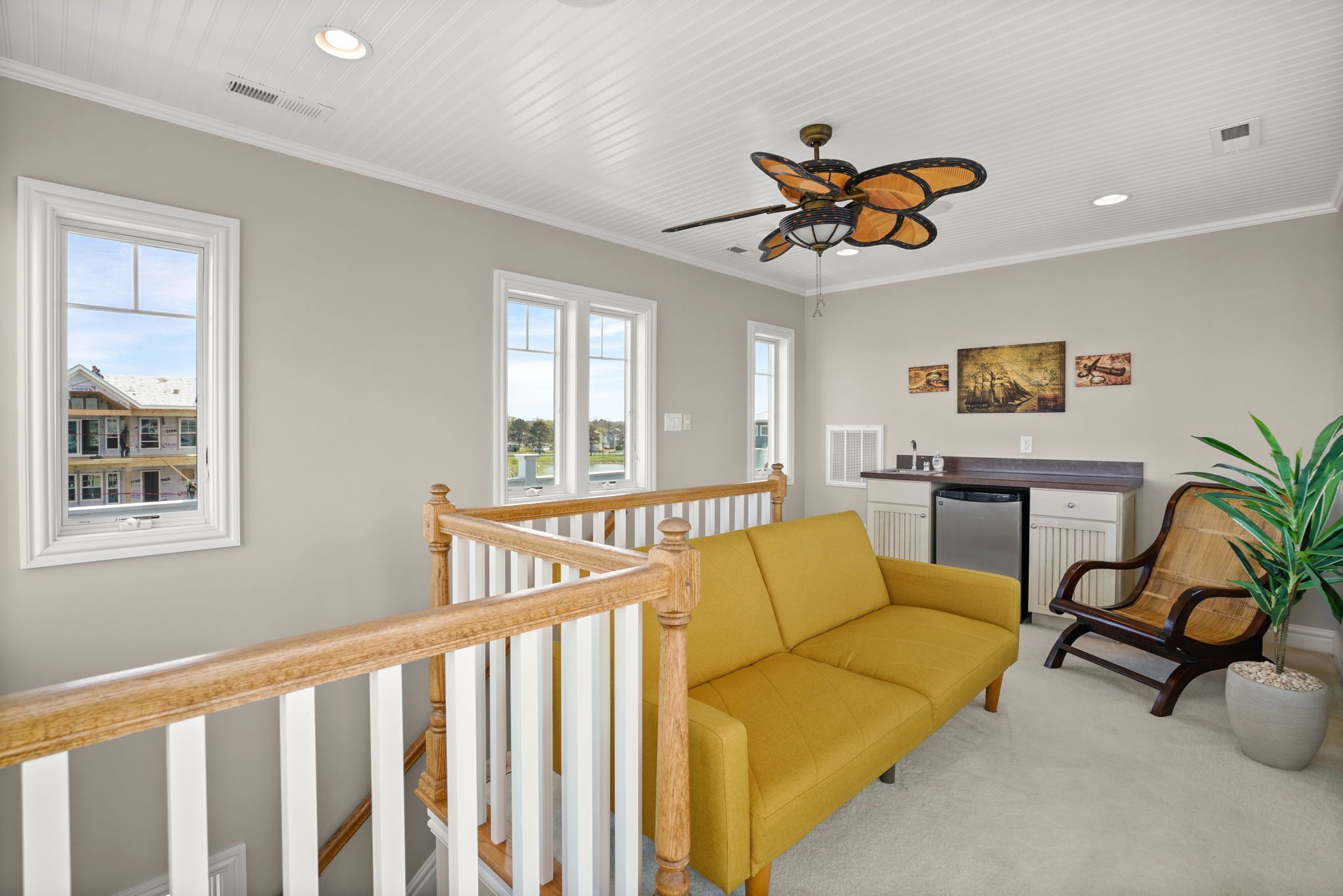 Un salon spacieux avec un canapé jaune, une chaise en bois et un ventilateur de plafond.
