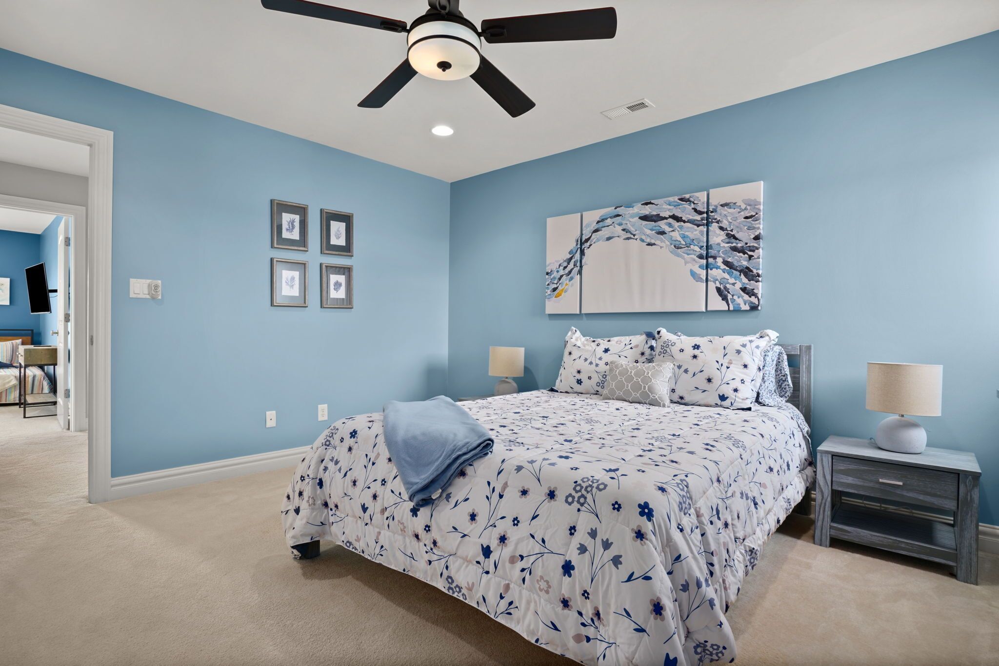 Un dormitorio con cama, mesitas de noche, ventilador de techo y obras de arte en la pared.