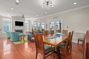 Un salon spacieux avec une cheminée, un coin repas avec des chaises en bois et un téléviseur fixé au-dessus de la cheminée.