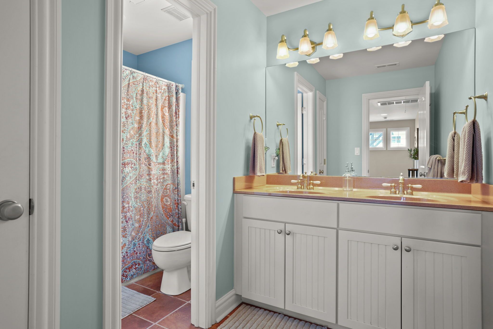 Une salle de bain avec un double lavabo, un grand miroir et un rideau de douche.