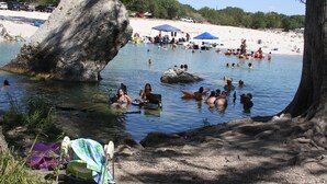 Une plage où l’on peut se baigner et bronzer, un grand rocher dans l’eau, et une rive sablonneuse avec quelques parasols et chaises.
