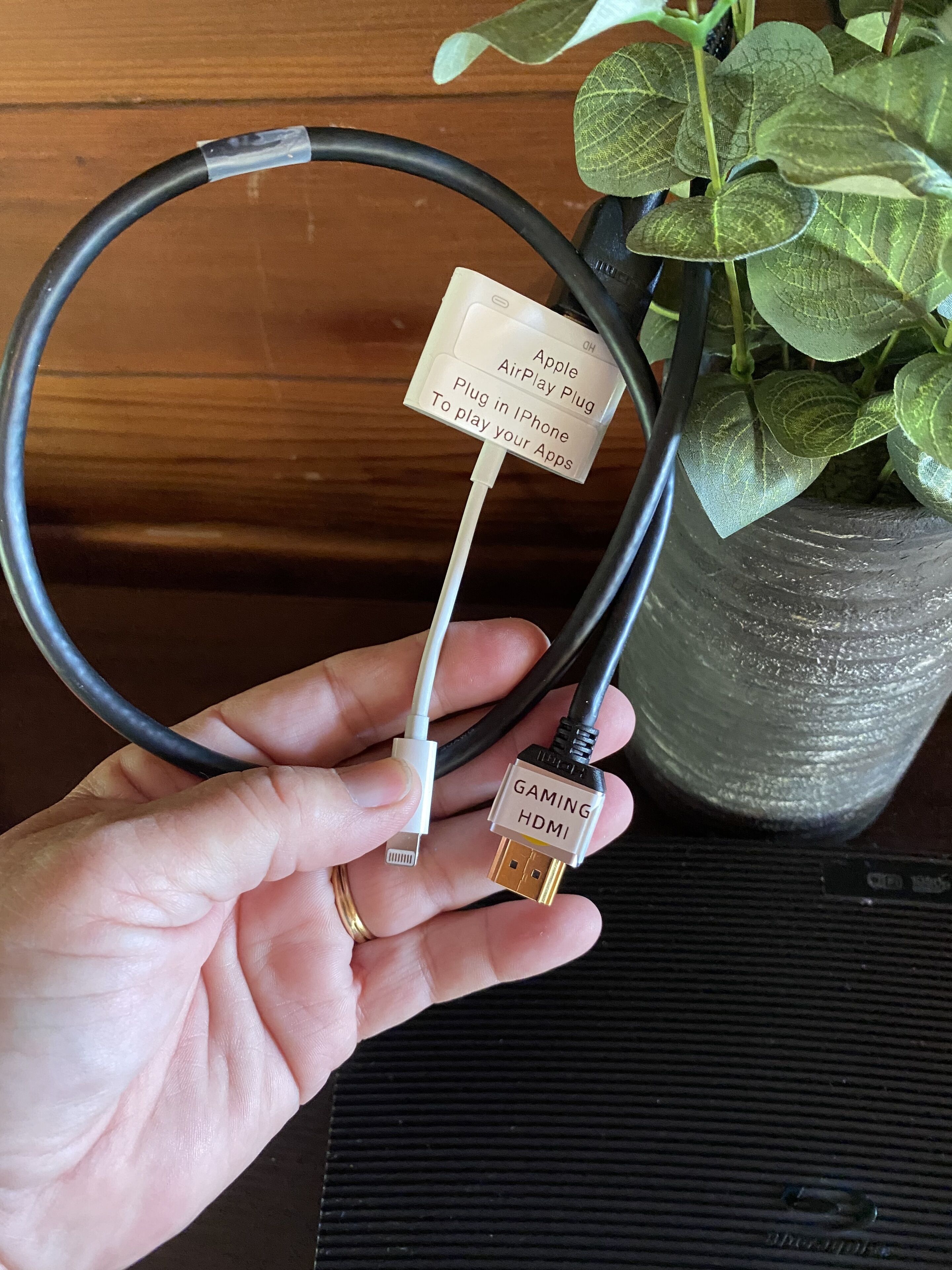 Käsi pitää Apple AirPlay -liitintä, ja siinä on etiketti, josta ilmenee, että se on tarkoitettu iPhone-laitteille ja pelien HDMI-liitäntään.