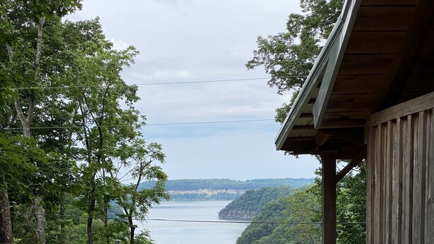 A wooden deck with a railing overlooking a body of water and forested hills. - 🤩 Charming Lake Side Retreat perched above scenic Faubush Creek.  (Nancy)