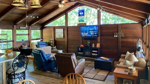 A cozy cabin interior with a wooden ceiling, a TV mounted on the wall, and a dining area with a table and chairs. - 🤩 Charming Lake Side Retreat perched above scenic Faubush Creek.  (Nancy)