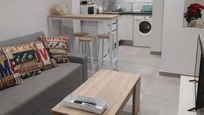 Ein modernes Wohnzimmer mit grauem Sofa, Holztisch und einer Küche im Hintergrund.