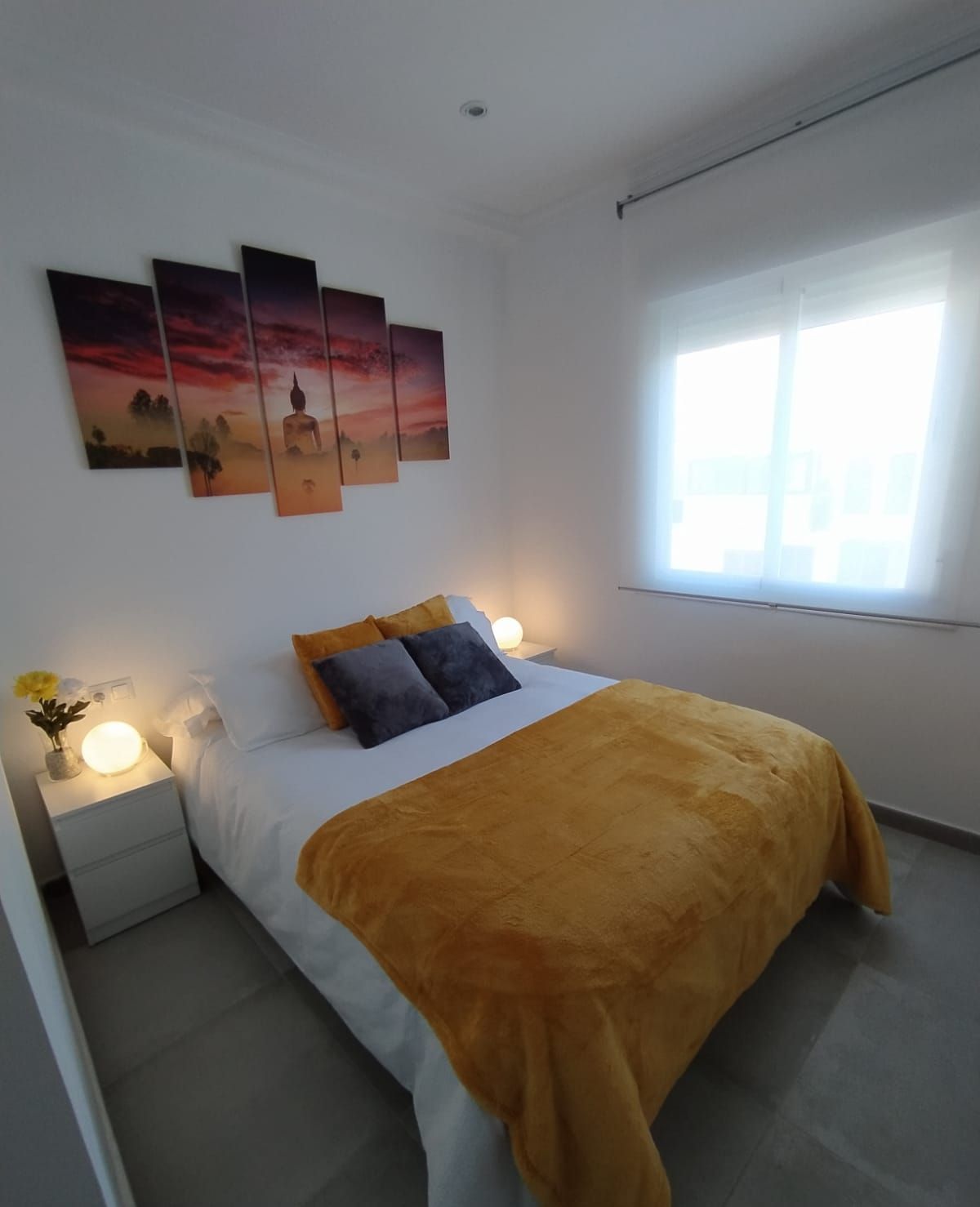 Un dormitorio con cama, mesitas de noche, lámpara y ventana.