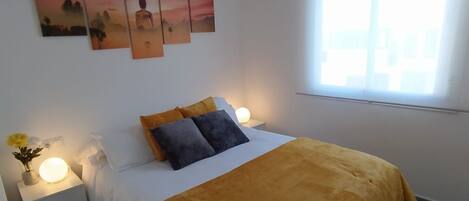 Un dormitorio con cama, mesitas de noche, lámpara y ventana.