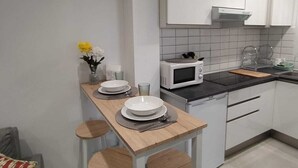Eine kompakte Küche mit weißen Schränken, einer Mikrowelle und einer kleinen Essecke mit Hocker.