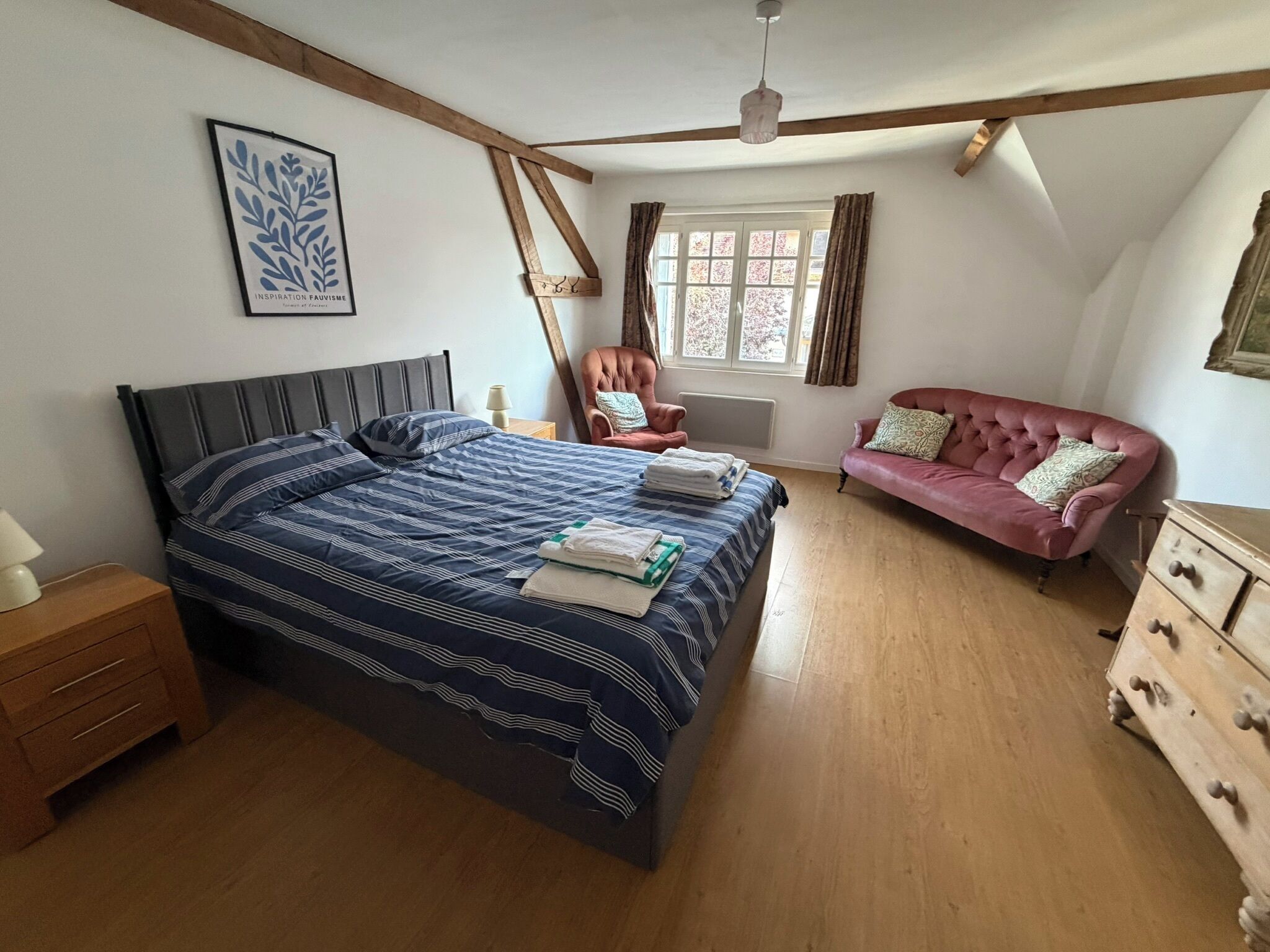 Une chambre à coucher comprenant un lit, une chaise, un canapé, une commode, une fenêtre et un ventilateur de plafond.