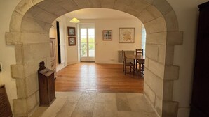 An arched hallway leading to a dining area with wooden flooring and a table with chairs.