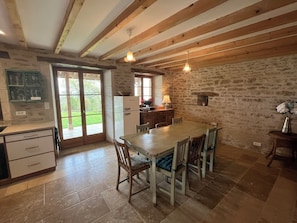 Eine rustikale Küche mit Steinwänden, Holzbalken, einem Esstisch mit Stühlen und einem Kühlschrank.